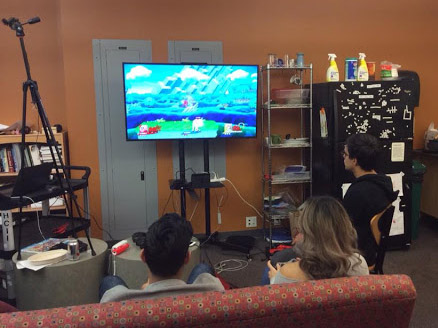 Three players playing super smash brothers on a couch. A camera is in the left corner.